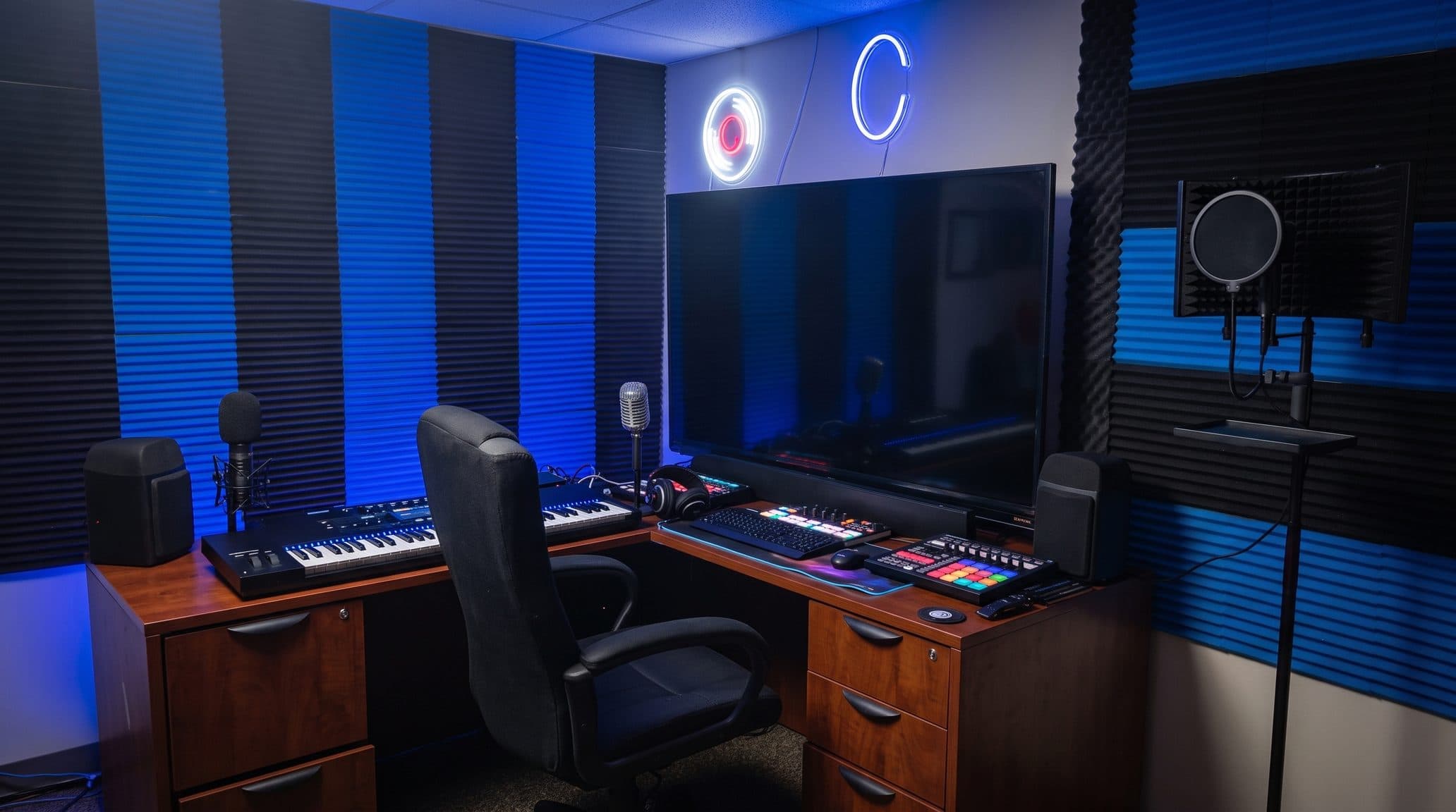 The music production studio with a MIDI keyboard, pad controller, studio monitors, headphones and a condenser microphone, surrounded by blue and black acoustic foam